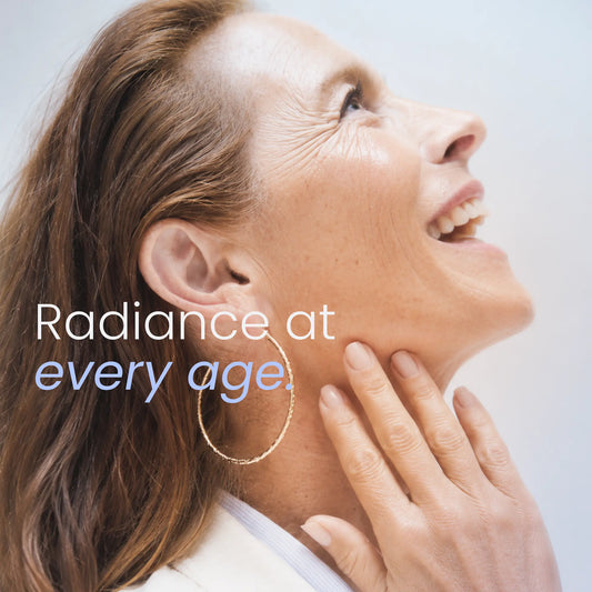 A close-up lifestyle shot of a smiling woman looking upward, touching her jawline, wearing a gold hoop earring and a white collared shirt. The text 'Radiance at every age.