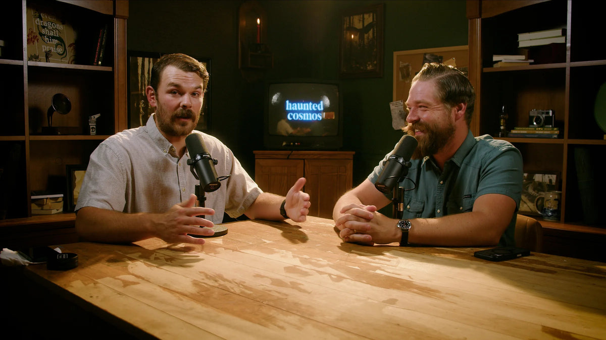 Two hosts talking at a table on the Haunted Cosmos set